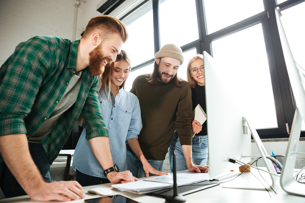Happy colleagues standing in office using computer