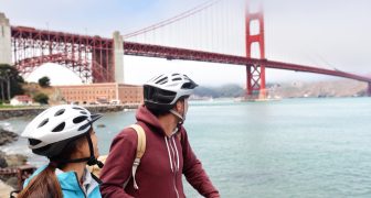 Golden gate bridge - biking couple sightseeing in San Francisco, USA. Young couple tourists on bike guided tour enjoying famous travel landmark in California, USA.