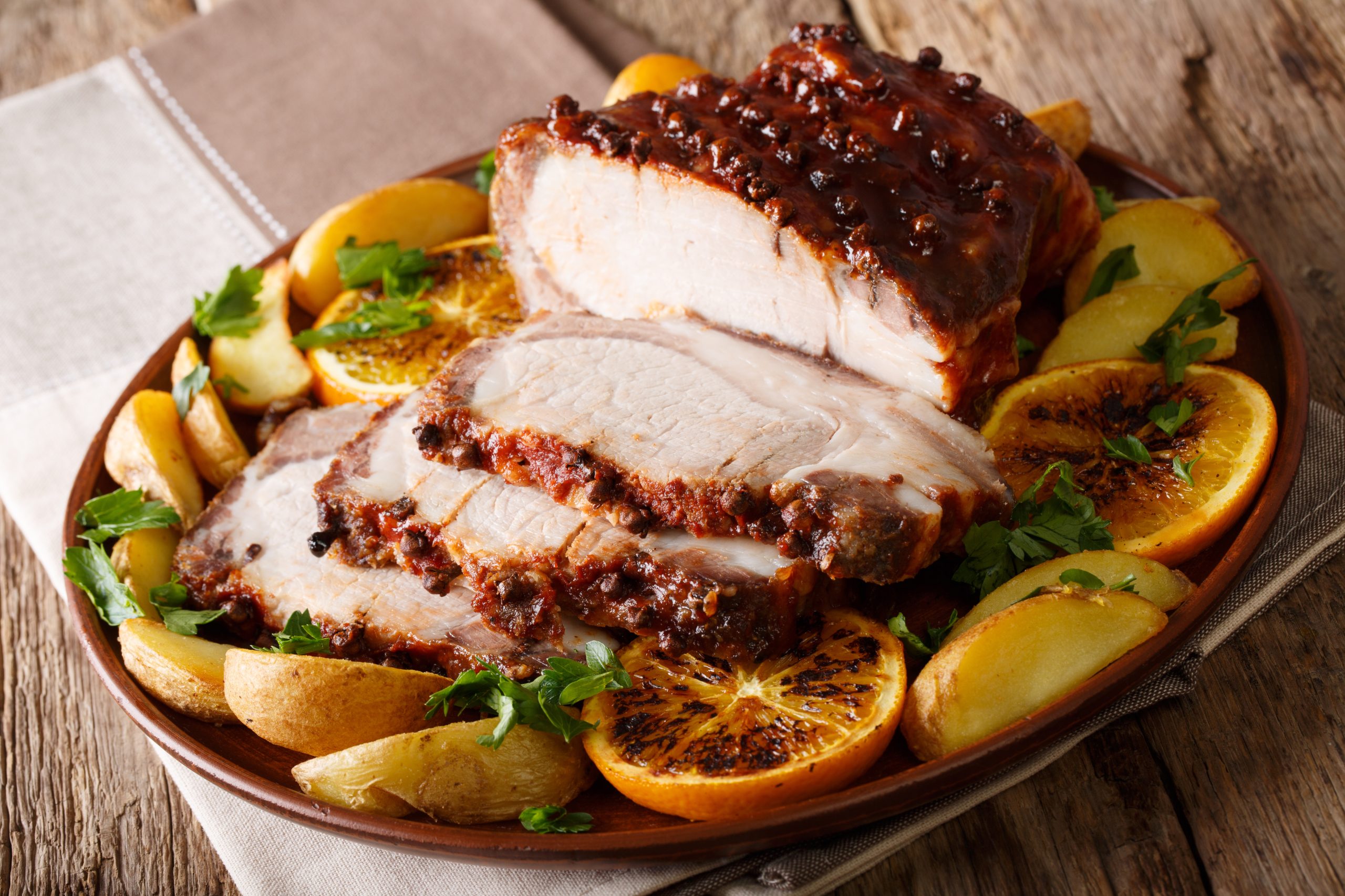 Christmas baked ham chopped slices with potatoes, oranges and apples close-up on a plate.  
