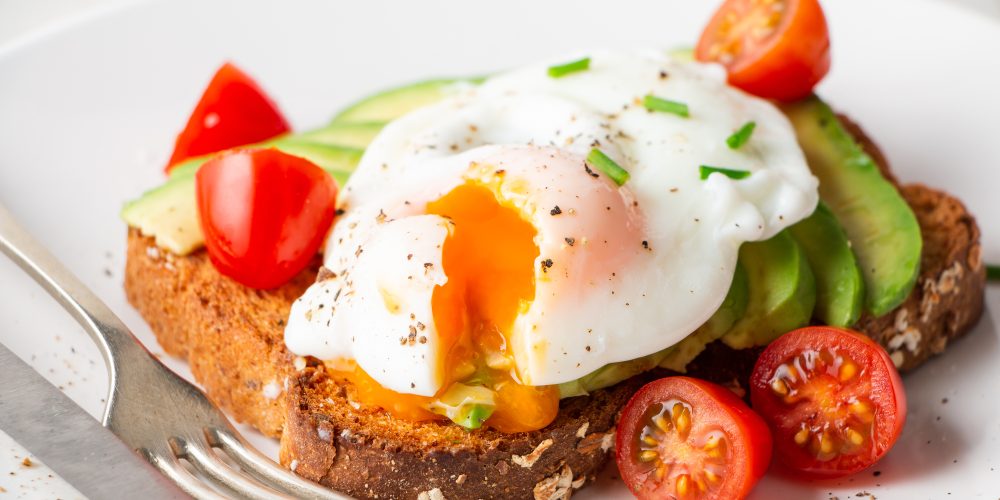 Healthy whole grain bread toast with avocado, poached egg, cherry tomato and baby leaves salad