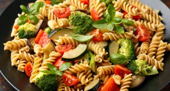 Fusilli pasta with vegetable, broccoli, zucchini, red pepper, eggplant, tomato and basil on black plate