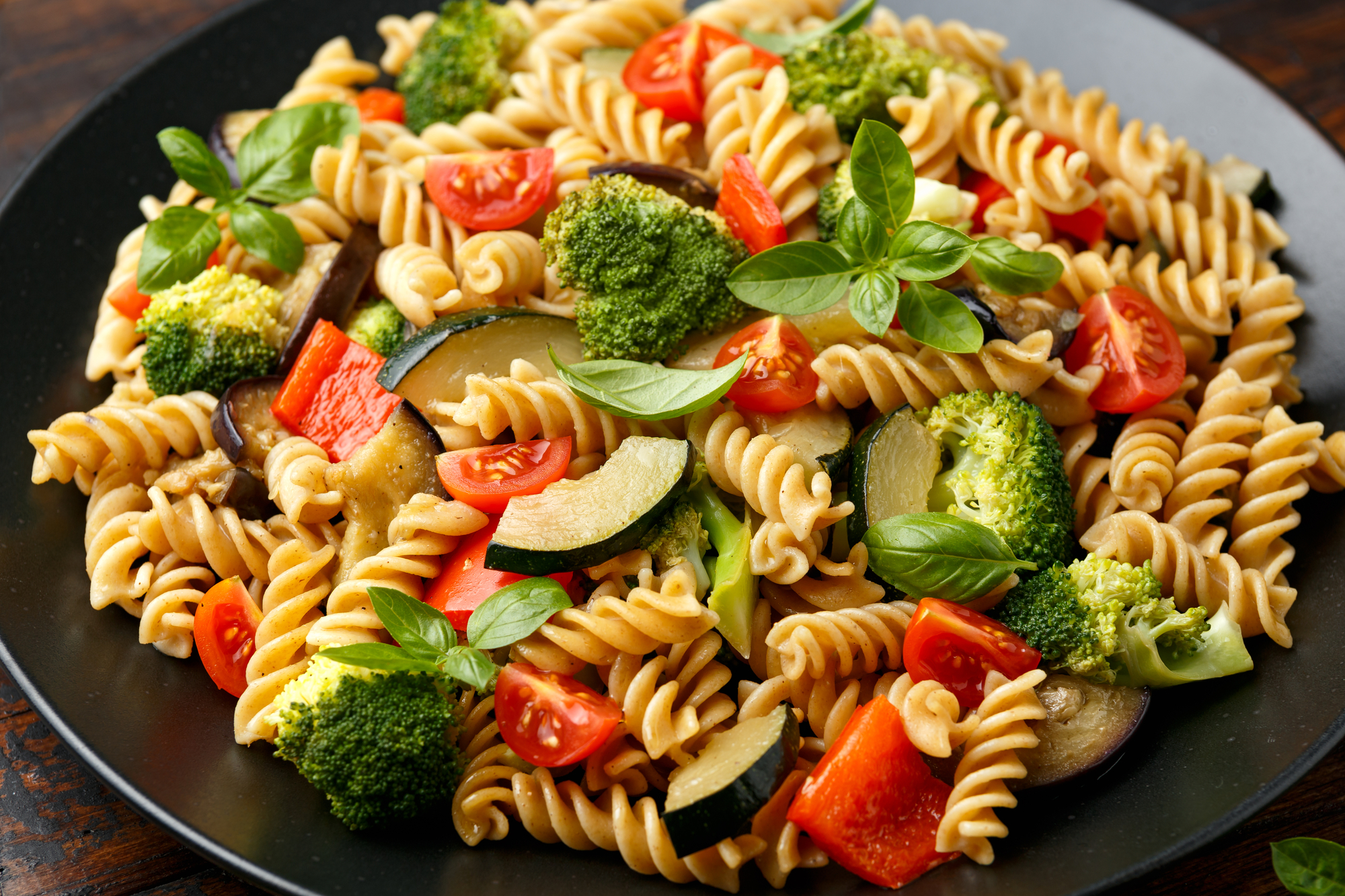 Fusilli pasta with vegetable, broccoli, zucchini, red pepper, eggplant, tomato and basil on black plate