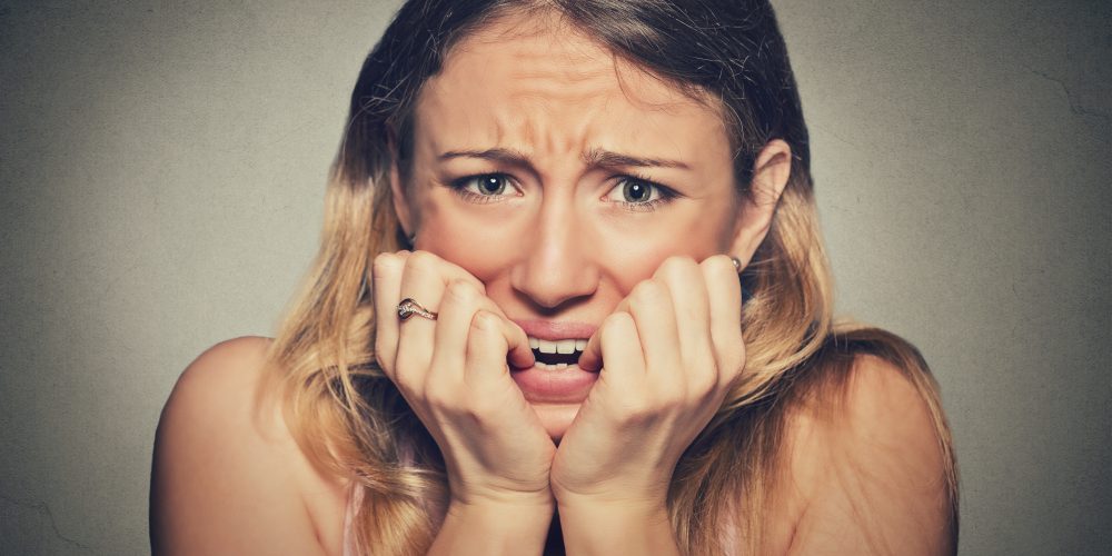 Closeup portrait headshot nervous stressed young woman girl student biting fingernails looking anxiously craving something isolated grey wall background. Human emotion face expression feeling