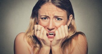 Closeup portrait headshot nervous stressed young woman girl student biting fingernails looking anxiously craving something isolated grey wall background. Human emotion face expression feeling