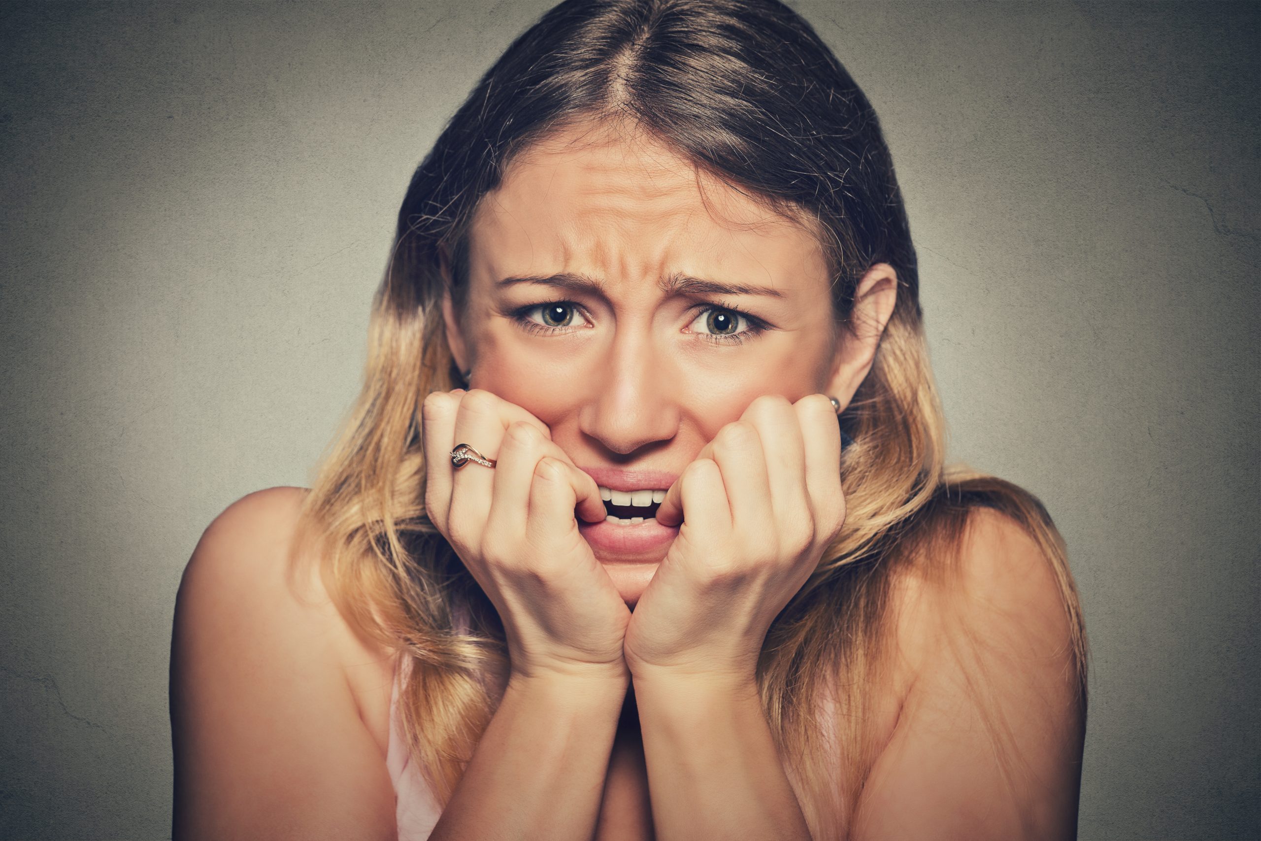 Closeup portrait headshot nervous stressed young woman girl student biting fingernails looking anxiously craving something isolated grey wall background. Human emotion face expression feeling