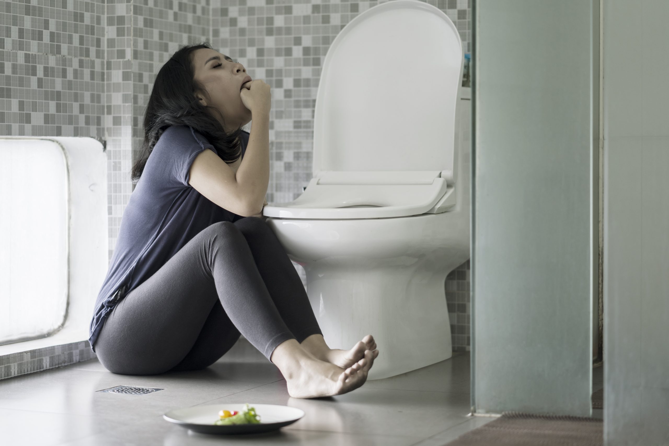 Picture of a young woman forcing herself to vomit with her fingers after eating in the bathroom. Eating disorder concept