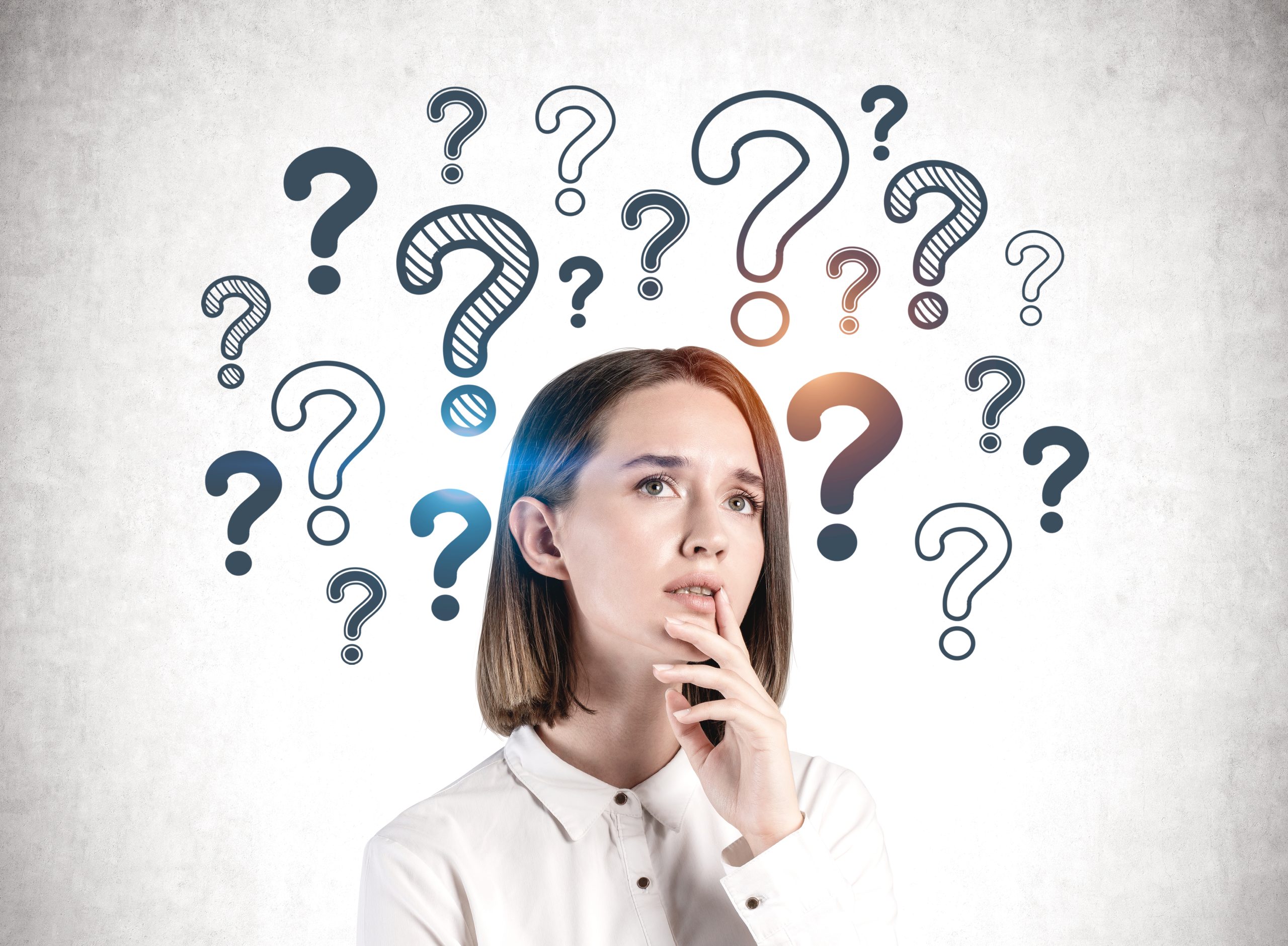 Concerned young European businesswoman standing near concrete wall with question marks drawn on it. Concept of choice and looking for answers